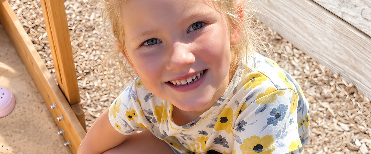 Smiling preschool child playing outdoors on a playground during a fun day at an early childhood education center.